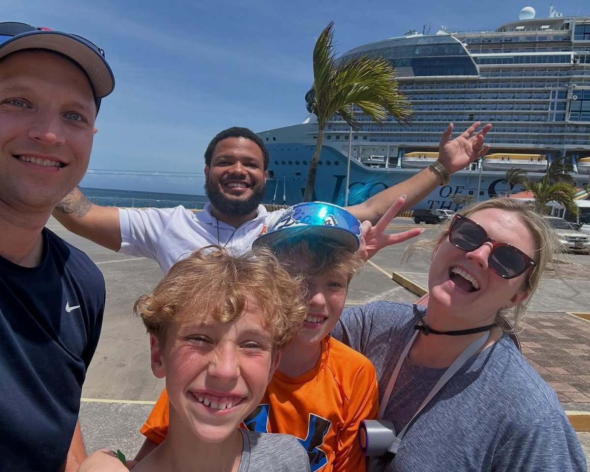 A family and their Island Breeze guide at the cruise port, ship behind them