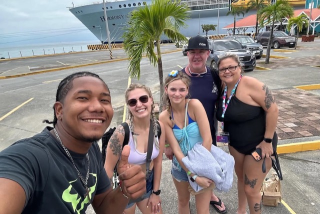 Guide and guests smiling in front of their cruise ship at the port