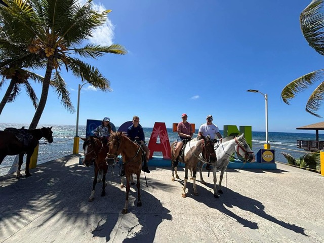 Horseback riders lined up at the ROATÁN sign by the sea