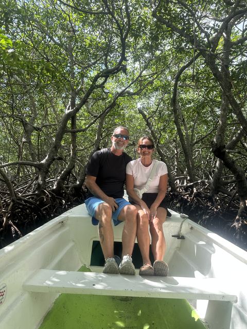 A couple seated in the bow of a boat under the mangrove canopy