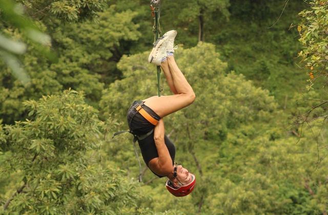 A guest riding the zipline upside down above the jungle canopy